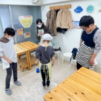 家族に見守られながら妹が床でうどん生地を踏んでいるところ 手打ちうどん作り体験教室 2025年11月 1.jpg – イリコスキー製麺所