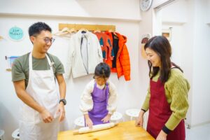 子どもが麺棒で生地をのばし、両親が近くで見守っている様子 手打ちうどん作り体験教室 2025年12月 A6407443-1.jpg – イリコスキー製麺所