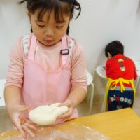 女の子が手のひらで生地を持ち、教室で集中して生地作りをする様子 手打ちうどん作り体験教室 2025年12月 A6407535-1-scaled.jpg – イリコスキー製麺所