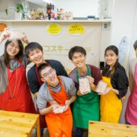 完成した紅いうどんのパックを持って笑顔で並ぶ大人数のグループ / A large group smiling and holding packs of freshly made red udon. 手打ちうどん作り体験教室 2025年12月 A6407628-1-scaled.jpg – イリコスキー製麺所