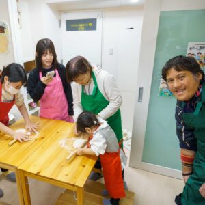 複数のテーブルで大人と子供が一緒に麺棒を使って生地を広げている様子。Adults and children working together with rolling pins to flatten the dough at multiple tables. 手打ちうどん作り体験教室 2026年1月 A6407755-1.jpg – イリコスキー製麺所