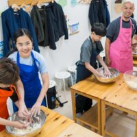 ボウルの中で粉と水を混ぜてうどんの生地作りをしている家族 A family mixing flour and water in bowls to make udon dough 手打ちうどん作り体験教室 2026年1月 A6408107-1-scaled.jpg – イリコスキー製麺所