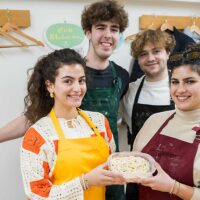 完成したうどんを持って笑顔でポーズをとる留学生やパレスチナからとおっしゃる若者4人組 A group of four young people including international students and a guest from Palestine smiling and posing with their finished udon 手打ちうどん作り体験教室 2026年1月 A6408163-1.jpg – イリコスキー製麺所