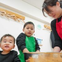 粉と水を混ぜて生地作りをするお兄ちゃんと、それを見守るお母さんと弟。 (Older brother mixing flour and water to make dough, watched by his mother and younger brother.) 手打ちうどん作り体験教室 2026年1月 A6408220-2-scaled.jpg – イリコスキー製麺所