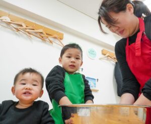 粉と水を混ぜて生地作りをするお兄ちゃんと、それを見守るお母さんと弟。 (Older brother mixing flour and water to make dough, watched by his mother and younger brother.) 手打ちうどん作り体験教室 2026年1月 A6408220-2.jpg – イリコスキー製麺所