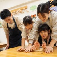 家族で協力して麺棒で生地を伸ばす様子(Family working together to roll out the dough with a rolling pin) 手打ちうどん作り体験教室 2026年1月 A6408363-1-scaled.jpg – イリコスキー製麺所
