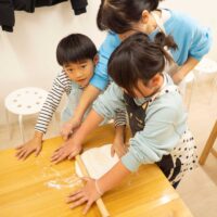 上から見た、子供たちが一生懸命生地を伸ばす場面(Top-down view of children working hard to roll out the dough) 手打ちうどん作り体験教室 2026年1月 A6408414-4-scaled.jpg – イリコスキー製麺所