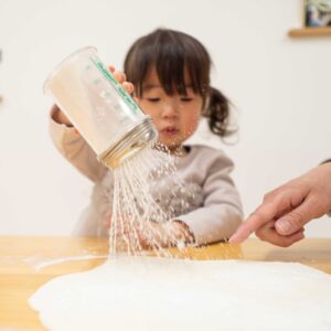生地に打ち粉を丁寧にふりかける女の子。 / The little girl carefully sprinkling dusting flour over the dough. 手打ちうどん作り体験教室 2026年2月 A6408524-1.jpg – イリコスキー製麺所