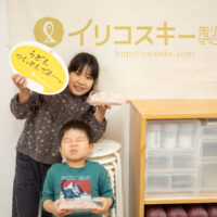 イリコスキー製麺所のバナーの前で、完成したうどんとフォトプロップスを持って記念撮影する子どもたち。 手打うどん作り体験教室 2026年3月 udon-class-kids-completed-noodles-iricosky-banner-1.jpg – イリコスキー製麺所