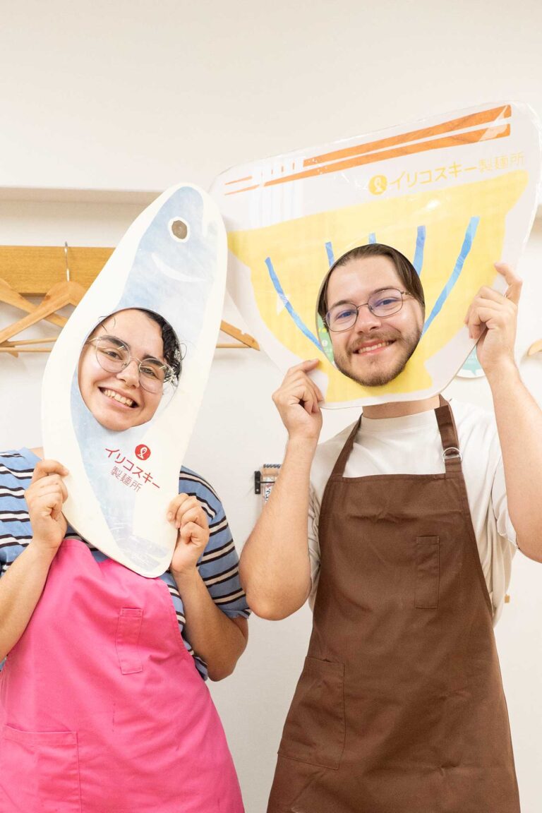 イリコスキー製麺所の顔はめパネルで笑顔の記念撮影。女性はいりこのパネル、男性はうどんのパネルに顔を出してにっこり。