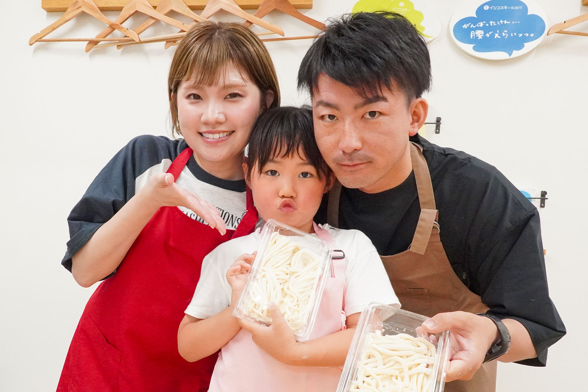 お父さん・お母さん・女の子の3人が完成したうどんの入ったトレーを持って笑顔で見せている。 手打ちうどん作り体験教室 2026年6月 udon-class-family-showing-finished-noodles-fathers-day.jpg – イリコスキー製麺所