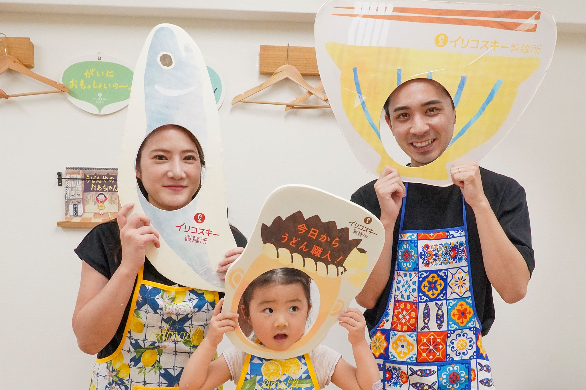 お父さん・お母さん・女の子の3人が顔はめパネルから顔を出して笑っている。 手打ちうどん作り体験教室 2026年6月 udon-class-family-three-face-cutout-panels.jpg – イリコスキー製麺所