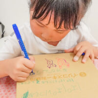 自分で打ったうどんを入れるギフトボックスに、女の子がカラーペンでメッセージやイラストを描いている。父の日のプレゼントづくり。 手打ちうどん作り体験教室 2026年6月 udon-class-girl-writing-fathers-day-gift-box.jpg – イリコスキー製麺所
